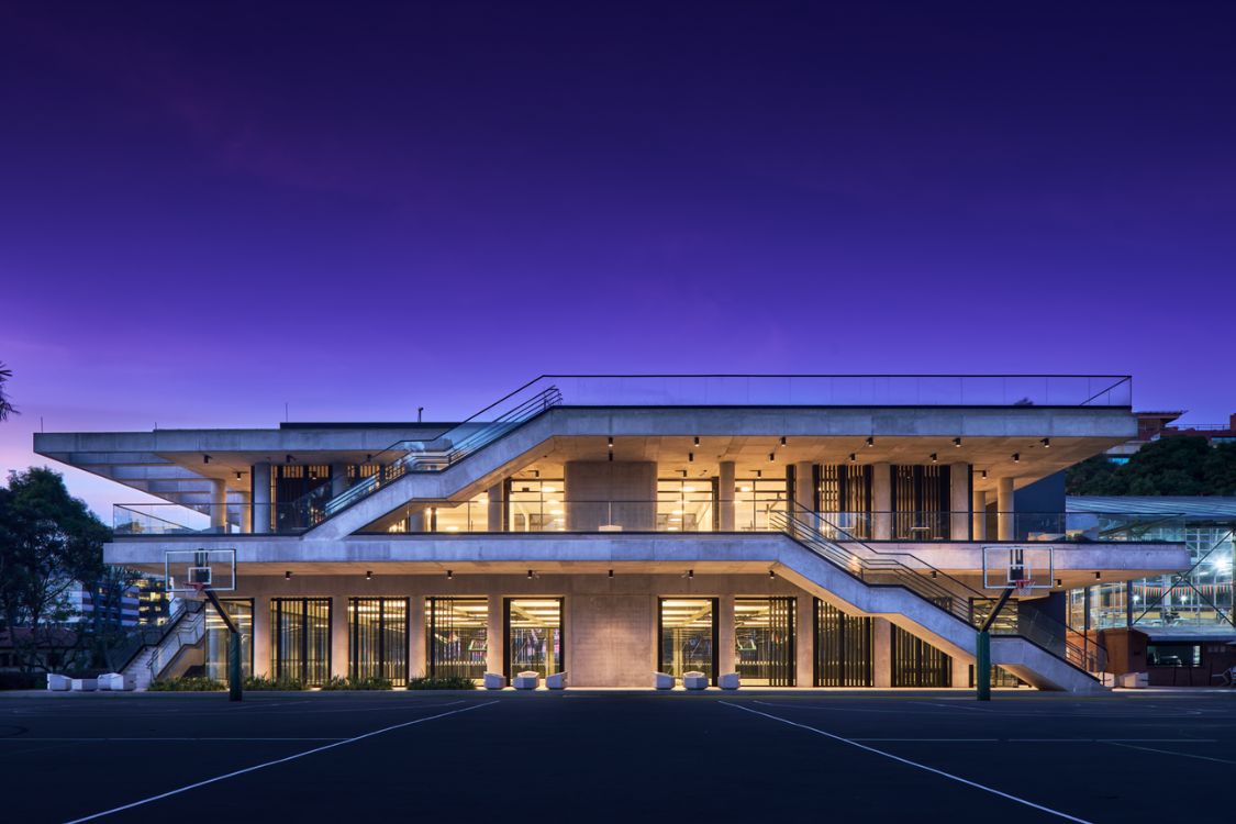 Gimnasio Moderno School Coliseum - Symmetrical illuminated facade with exposed concrete waffle ceiling at dusk - Felipe Gonzalez Pacheco.jpg